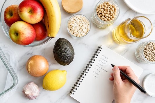 healthy postpartum grocery staples with a shopping list: apples, banana, avocado, oats and seeds on a marble counter